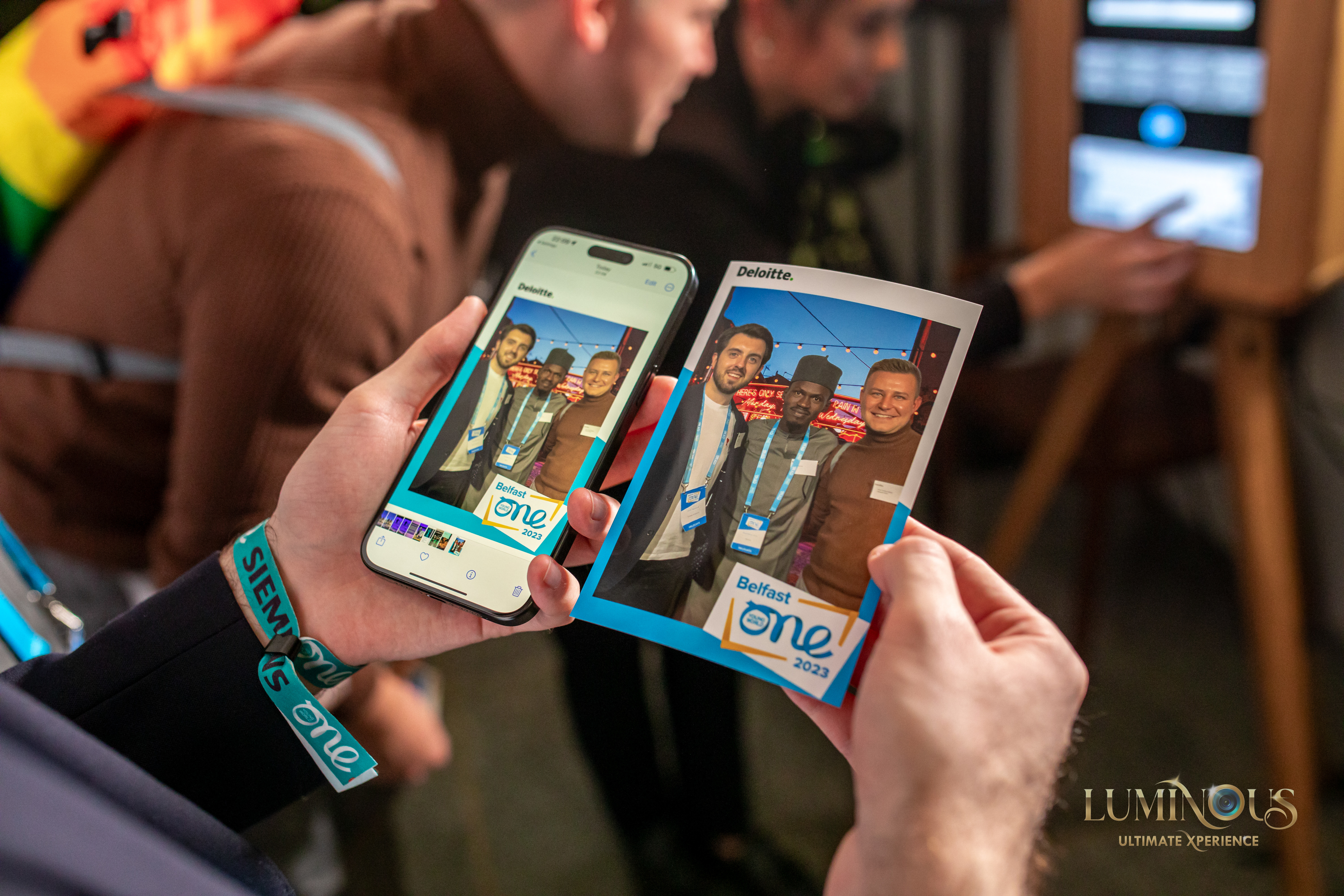 Gents at a corporate event showing copies of photos they had taken on the Everybooth, sent to a mobile phone and printed out