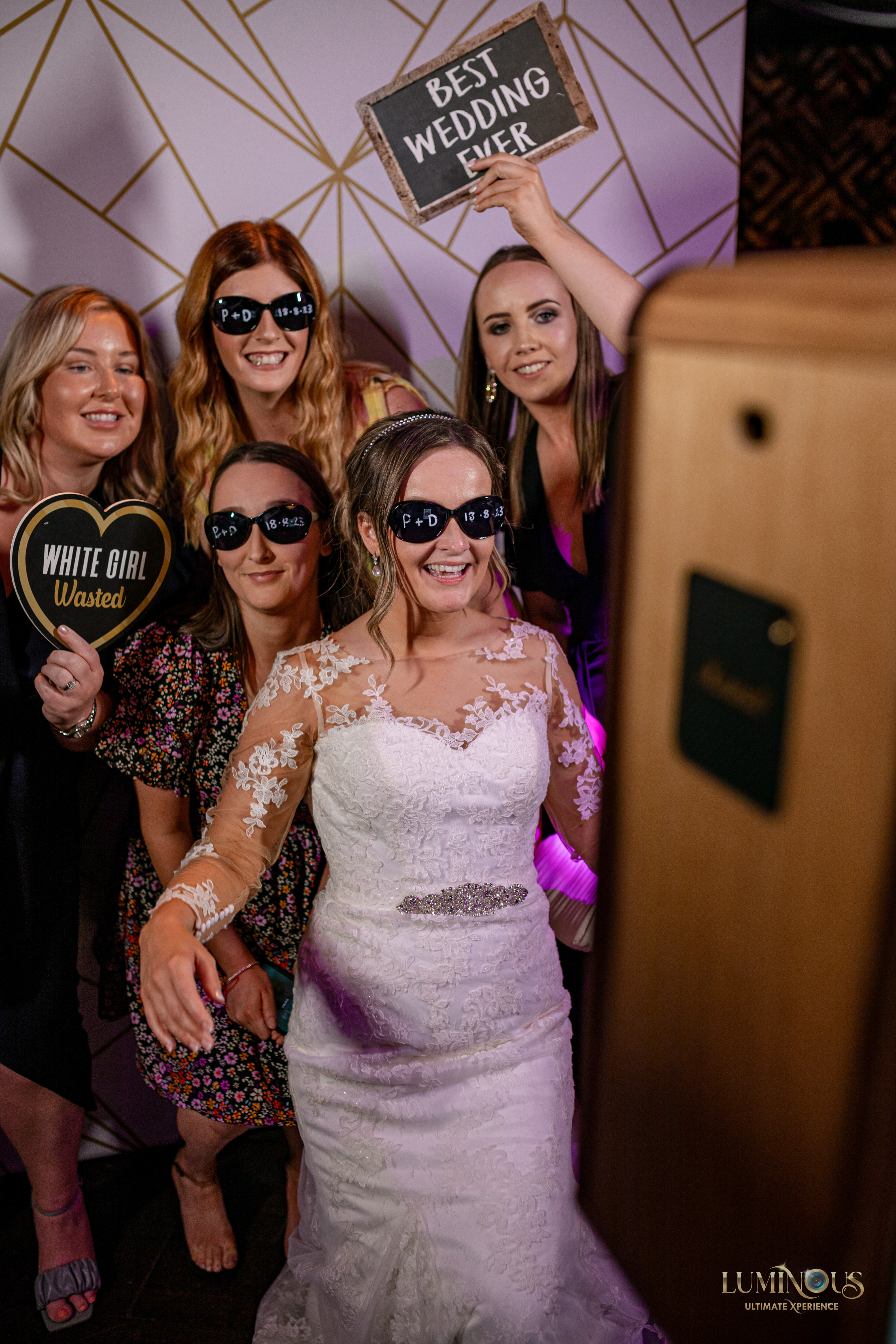 Ladies at a wedding getting their photos taken on the Everybooth with the Bride, in front of a backdrop using signboards and props